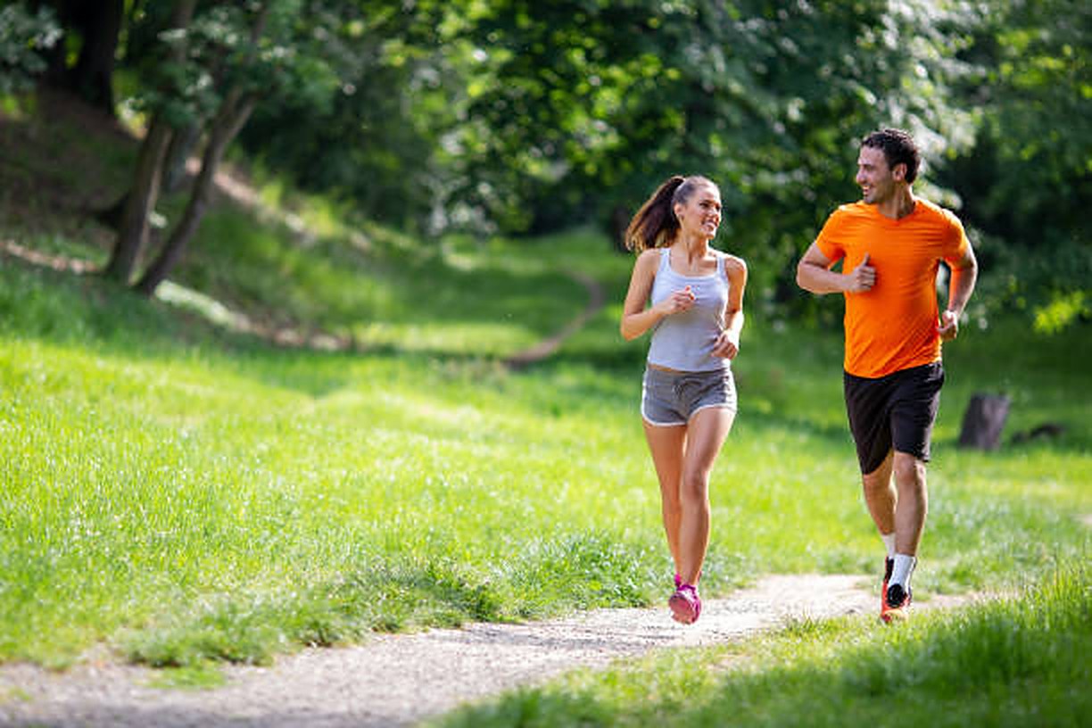 Two runners jogging side by side on a park trail, smiling at each other